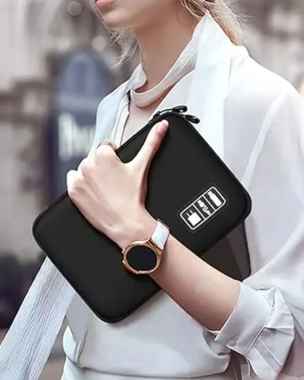 Person holding a black clutch with a brand logo, blurred background